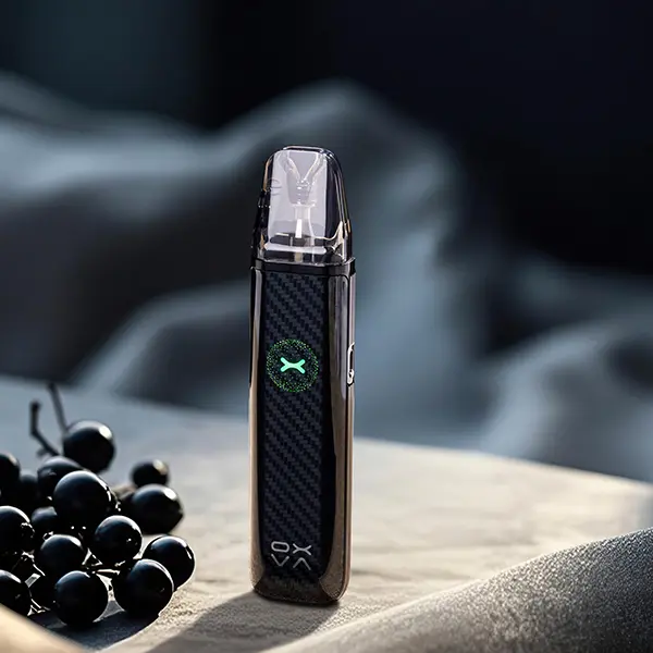 Oxva Xlim Go 2 Pod Kit in Schwarz mit Carbon-Optik und Pod, seitlich vor dunklem Hintergrund mit Beeren